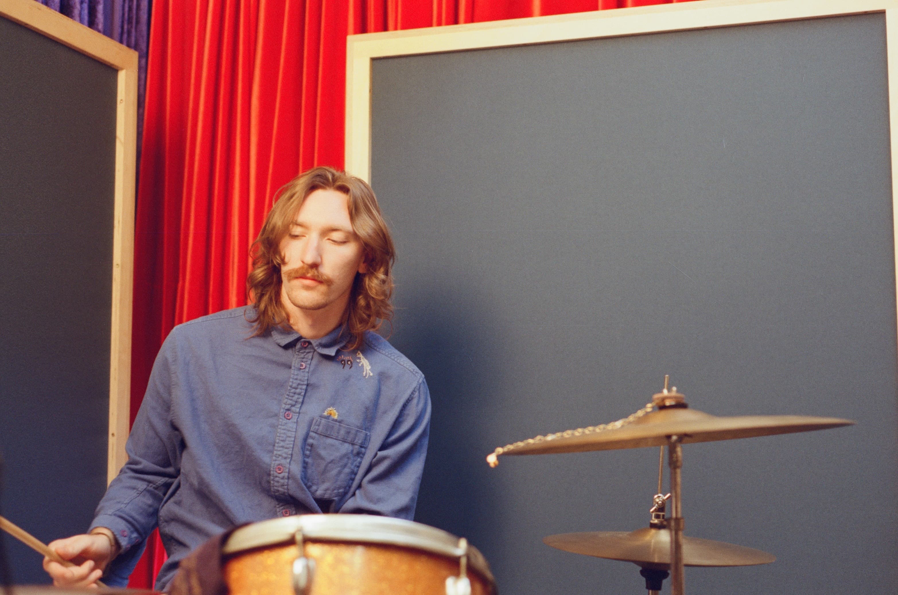 Kaden Smith playing drums in front of deep red curtains.