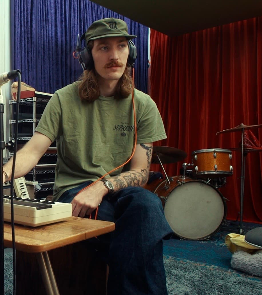 Kaden Smith in the studio with headphones and drum kit in the background.